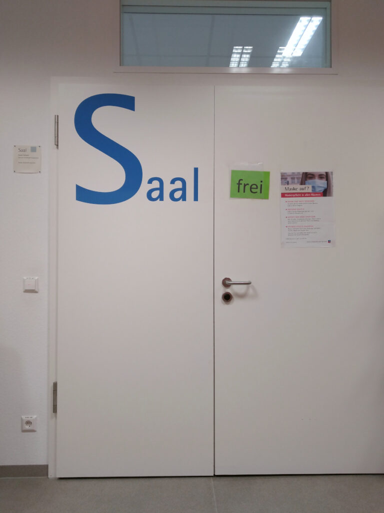 Tür zum Saal mit großem Schriftzug "Saal" in blauer Schrift auf weißem Hintergrund.