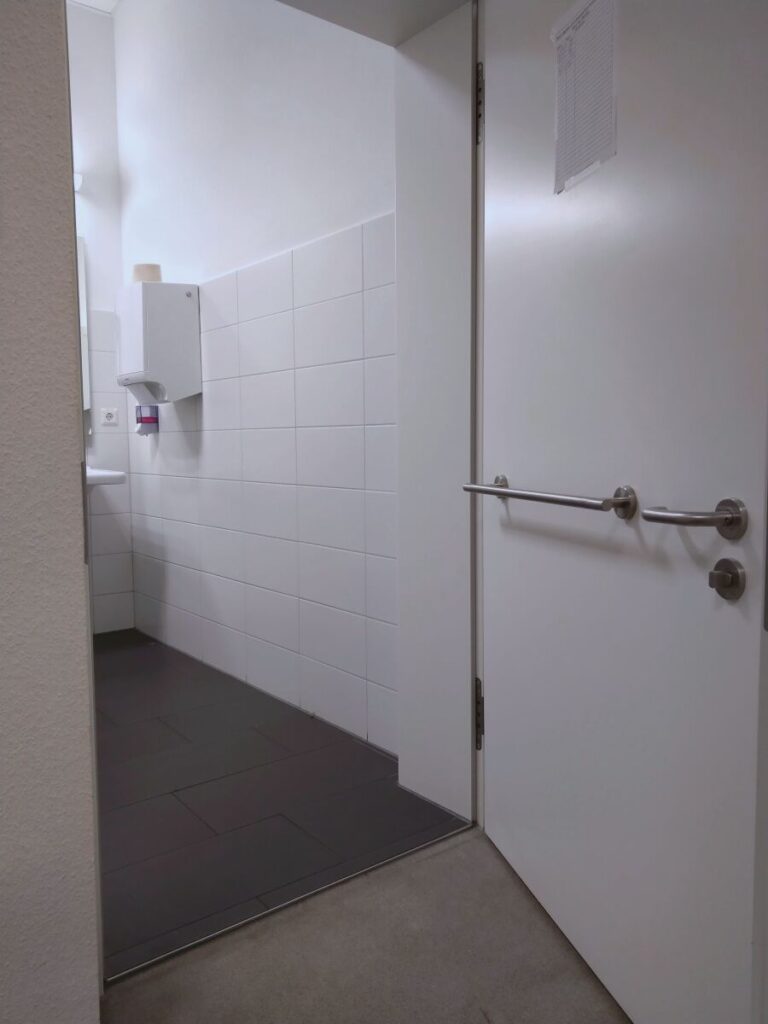 Zugang zur barrierefreien Toilette: Tür mit niedrigem Griff und innen einer Zuzieh-Stange.