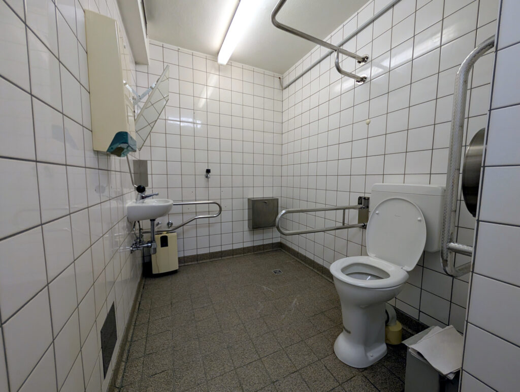 Barrierefreie Toilette: WC vorne rechts, Waschbecken hinten links.