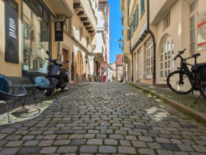 Mittelalterliche Gasse mit unebenem Kopfsteinpflaster, gesäumt von hohen, dicht stehenden Häusern, die eine einengende Atmosphäre schaffen.