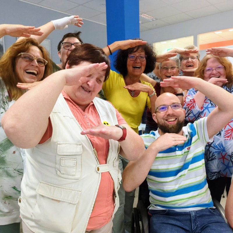 Gruppenbild mit 8 lachenden Personen. Darunter eine blinde Frau und ein Rollstuhlfahrer.