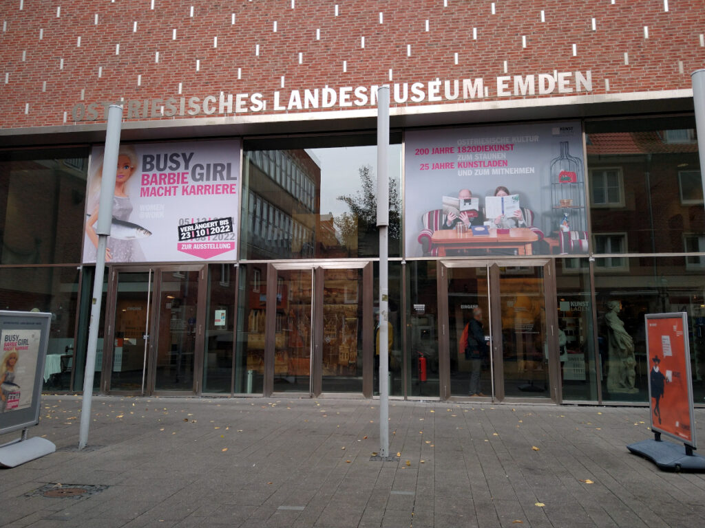 Blick von außen auf den Eingang des Landesmuseums: Glastüren in einem roten Backsteingebäude, darüber Plakate zur aktuellen Ausstellung.