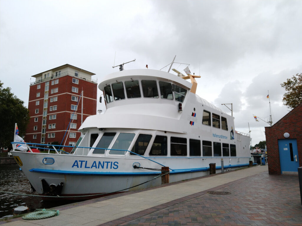 Zweistöckiges Schiff mit dem Namen "Atlantis" am Bug, am Hafen vertäut.