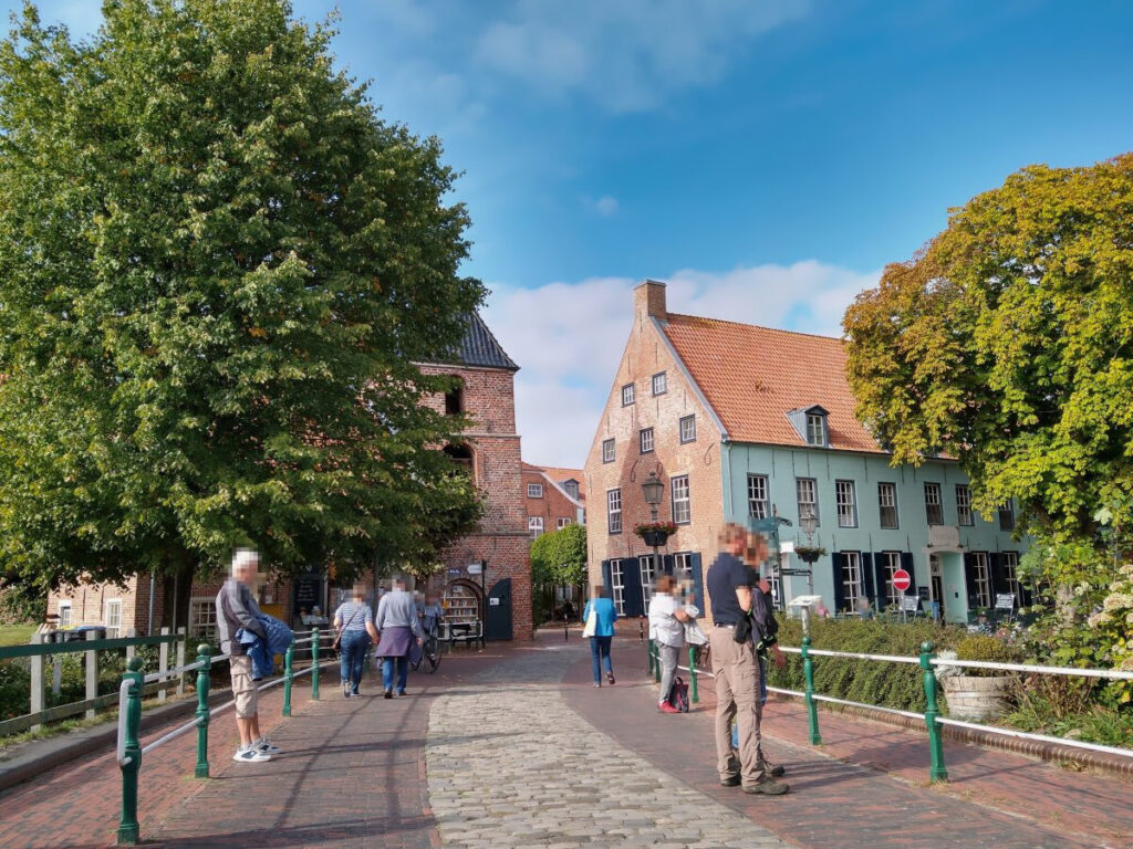 Fußgängerzone mit einer Brücke über den Kanal. Von einem Zaun abgegrenzt auf beiden Seiten der Brücke verlaufen Fußwege. In der Mitte der Straße ist ein Streifen aus historischem, unebenem Kopfsteinpflaster, während der äußere Bereich der Straße mit ebenem Pflaster bedeckt ist.