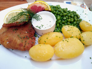 Teller mit paniertem Fisch, Kartoffeln, Erbsen und einem Schälchen mit Dip.