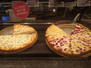 2 Kuchen-Platten mit verschiedenen Käsekuchen in einer Glas-Vitrine.