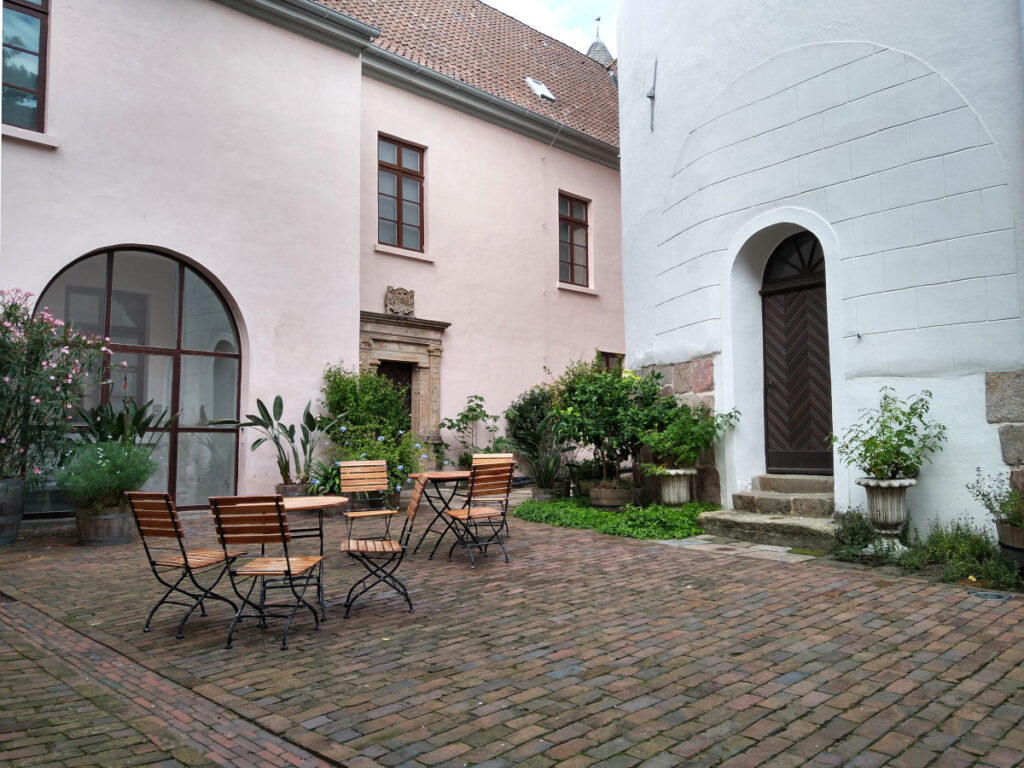 Innenhof mit historischem Kopfsteinpflaster, zwei Tischen mit Stühlen und mehreren Kübelpflanzen. Rechts befindet sich der Eingang zum Schlossturm.