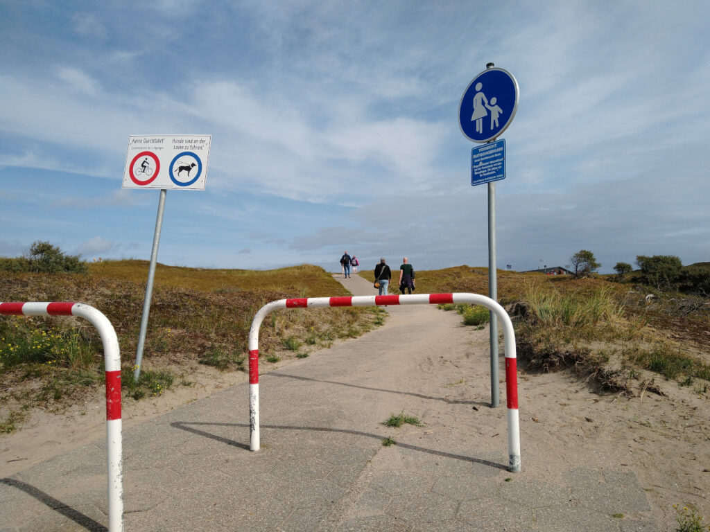 Asphaltierter Weg über die Düne, am Anfang des Weges eine Umlaufschranke.