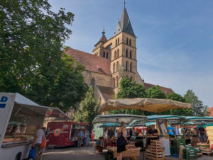 Wochenmarkt mit Ständen voller Obst und Gemüse. Im Hintergrund die gotische Stadtkirche mit ihren 2 Türmen.