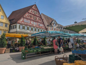 Wochenmarkt mit Ständen voller Obst und Gemüse. Im Hintergrund ein wunderschönes Fachwerkhaus.